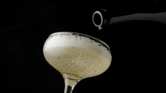 Close-up, slow motion shot: Pouring champagne into a glass on a black background