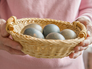 Painted eggs in wicker wooden basket in hands of woman