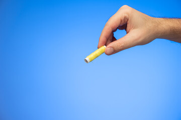 Small reel of yellow sewing thread held in hand by Caucasian male hand studio shot isolated on blue background