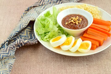Gado-gado, traditional Indonesian salad with peanut sauce on brown background