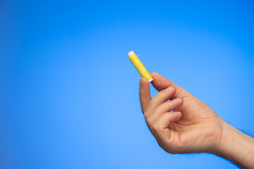 Small reel of yellow sewing thread held in hand by Caucasian male hand studio shot isolated on blue background