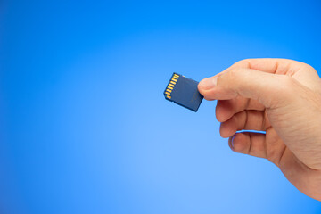 Small plastic SD memory card held in hand by Caucasian male hand studio shot isolated on blue background