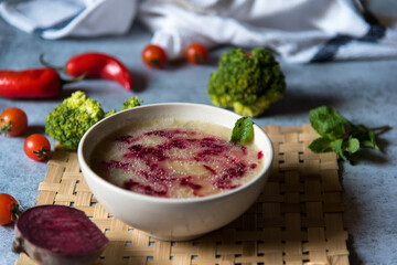 Healthy food chicken and beetroot soup in a bowl along with raw condiments on a background with use of selective focus.