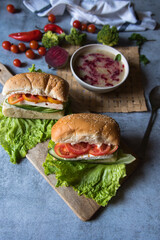 Close up of  submarine sandwich with ham and vegetables on a wooden platter.