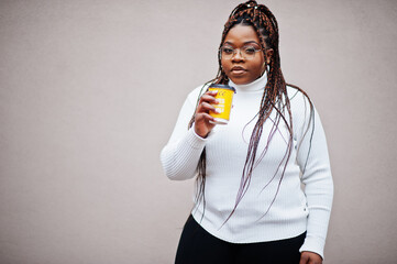 Glamorous african american woman in white turtleneck sweater pose at street with cup of coffee at hand.