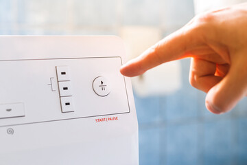 Start/stop button on washing machine, man's finger about to push it