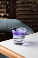 purple cocktail in transparent short glass with whole ice cube on the table at restaurant