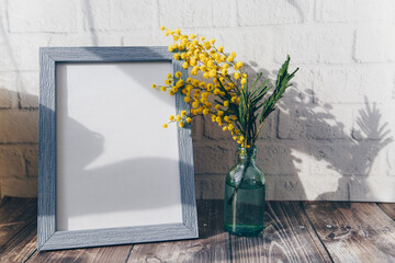 Photo frame and a small bottle with mimosa on a brick wall background. spring concept