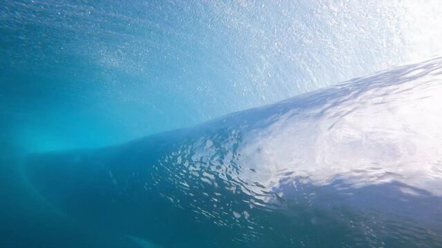 Dramatic underwater of a large ocean wave rolling and breaking, with dark blue water and illuminated bubbles - Oahu, Hawaii