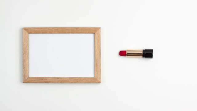 Stop motion animation mockup flat lay of bright wooden frame and red lipstick in gold black shell of the right side of the image with copy space for your text on white background. Beauty and fashion