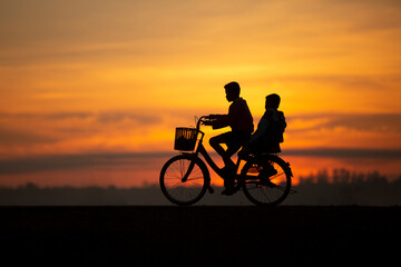 Obraz na płótnie Canvas The boys riding the bicycle during the evening with the background of sunset in summer. Both child feeling happiness with his lifestle