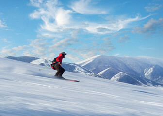 Fototapeta na wymiar Man in red jacket skiing down slope in bright sunshine