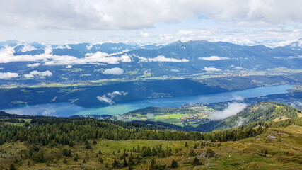 Fototapeta premium A panoramic view on the Millstaettersee from Granattor in Austrian Alps. The distant lake is surrounded by high mountains. There are few clouds above the lake and the valley. Endless mountain chains