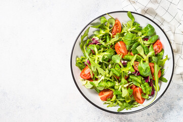 Green salad with arugula, lamb and tomatoes. Healthy vegan dish. Top view at white table.
