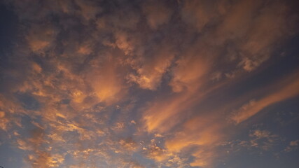 A clear blue sky with clouds that flush red as the sun sets.