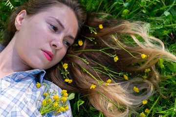 Naklejka premium Concept of hair caring.Young woman lying on green grass field with blonde hair with tiny yellow flowers in it.