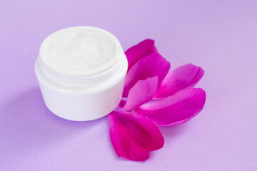 Obraz na płótnie Canvas White moisturizing cream with peony extract and petals nearby it on pink background
