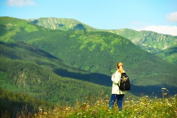 Fototapeta na wymiar Girl tourist with a backpack for walks admires the views in the mountains. beautiful mountain summer green landscape with green mountains and blooming meadow. 