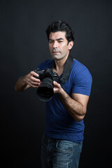 fotografo moro in maglietta blu e fotocamera al collo è pronto a fare una foto  , isolato su sfondo nero
