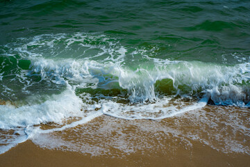 The blue sea waves lapping yellow sands and clear green water. 