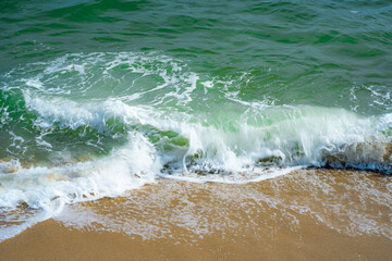 The blue sea waves lapping yellow sands and clear green water. 