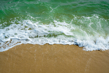The blue sea waves lapping yellow sands and clear green water. 