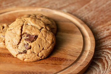 Delicious Homemade Chocolate Chip Cookies. Chocolate chip cookies on plate on wooden background. Warm, golden brown, chocolate chip cookies cooling on baking paper. Natural handmade organic cookies.