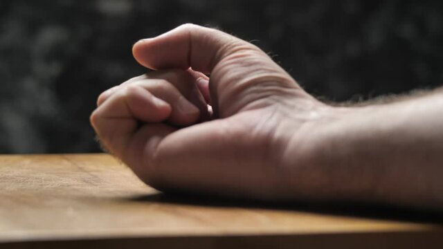 A fist clenches on the table in a gesture of anger. A male hand shows emotions in an expressive light.