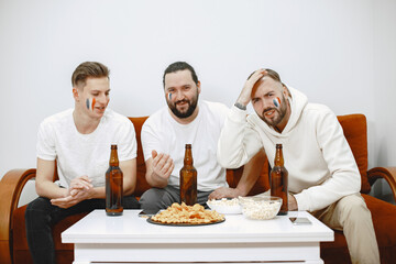 Fans sitting on the couch in the living room. Guys drinking a beer.