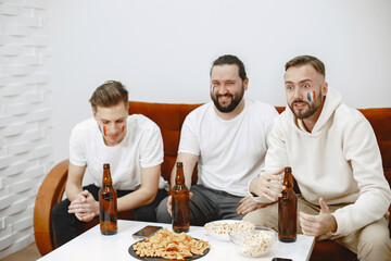 Fans sitting on the couch in the living room. Guys drinking a beer.