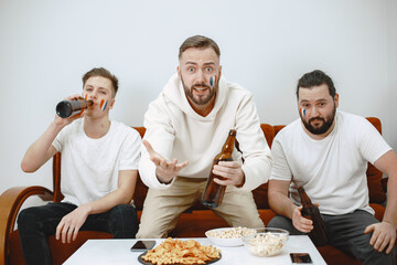 Fans sitting on the couch in the living room. Guys drinking a beer.