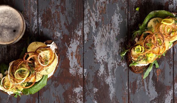 Sandwich with rye bread, butter, potatoes, sauce and crispy onions on a dark wooden background top view. Scandinavian cuisine. Easy and tasty lunch, dinner or beer snack. Free space for text. Rustic 