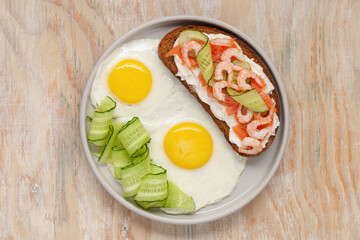 Sandwich with cheese, salmon, cucumber and shrimp, fried eggs on a plate and coffee on the table. Healthy breakfast. Top View