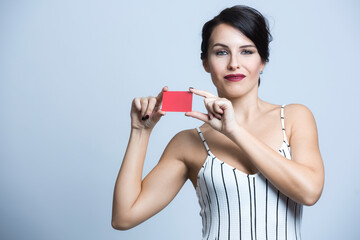 Donna bianca con i capelli neri  vestita  con una tuta bianca a righe mostra una card rossa ,...