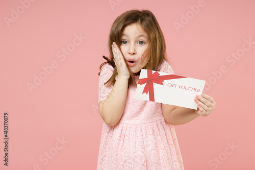 Little kid girl 5-6 years old wears rosy dress have fun hold gift certificate voucher store isolated on pastel pink background child studio portrait. Mother's Day love family people lifestyle concept.