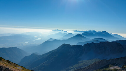 Panoramic view on the haze shrouded valley from the way to Mittagskogel in Austrian Alps. Clear and sunny day. Endless mountain chains. Outdoor activity. Barren top of the mountains, lush lower parts
