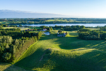 Hilly landscape pictured from a drone. A large lake and country houses on a sunny summer day.
