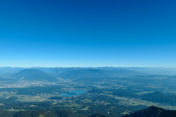 A panoramic view on the Alps from the top of Mittagskogel in Austrian Alps. Clear and sunny day. There is a lake at the bottom. A bit of haze in the valley. Outdoor activity. Alpine mountain chains
