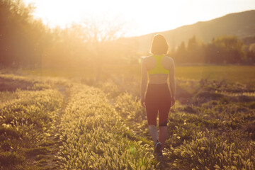 Fototapeta premium View of woman from behind with sportswear, walking on country road, portrait