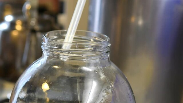 Moonshine flows in a thin stream into the jar during distillation. Moonshiner prepares strong alcohol at home. 