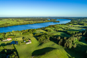 A large lake with blue water surrounded by numerous hills, forests and fields on the landscape from a drone.
