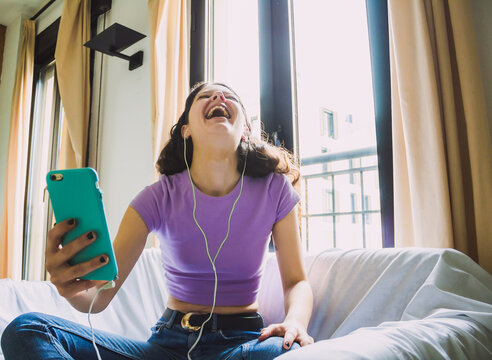 happy young woman making video call at home wearing headphones on sofa