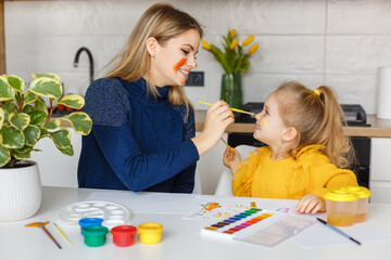 Mother and daughter painting at home. Cute little kid in yellow sweater having fun with parent and...