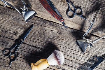 On a rustic wooden weathered surface are old barber tools. Vintage manual hair clipper comb razor...