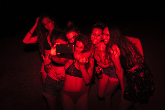 Group of young women having fun at a lakeside party at night with a red light