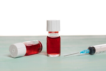 medical vaccine vials with red liquid and syringe over green table and white background....
