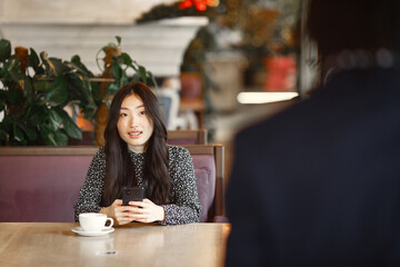 Chinese girl with phone. Black guy is preparing a surprise. Happy girl at the table