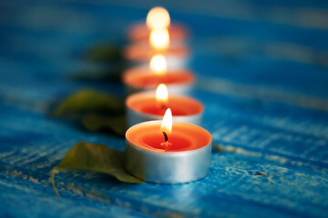 Light orange candles used for aromatherapy, placed on green leaves and blue wooden background, creating a blurred effect in an enchanting environment