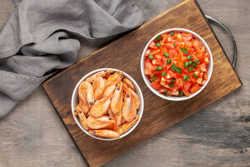 Boiled shrimp prawns in a shell  in a bowl and tomatoes on a wooden background. Top view