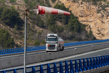 Tank truck with dangerous goods circulating through a viaduct and an windsock indicating that there...